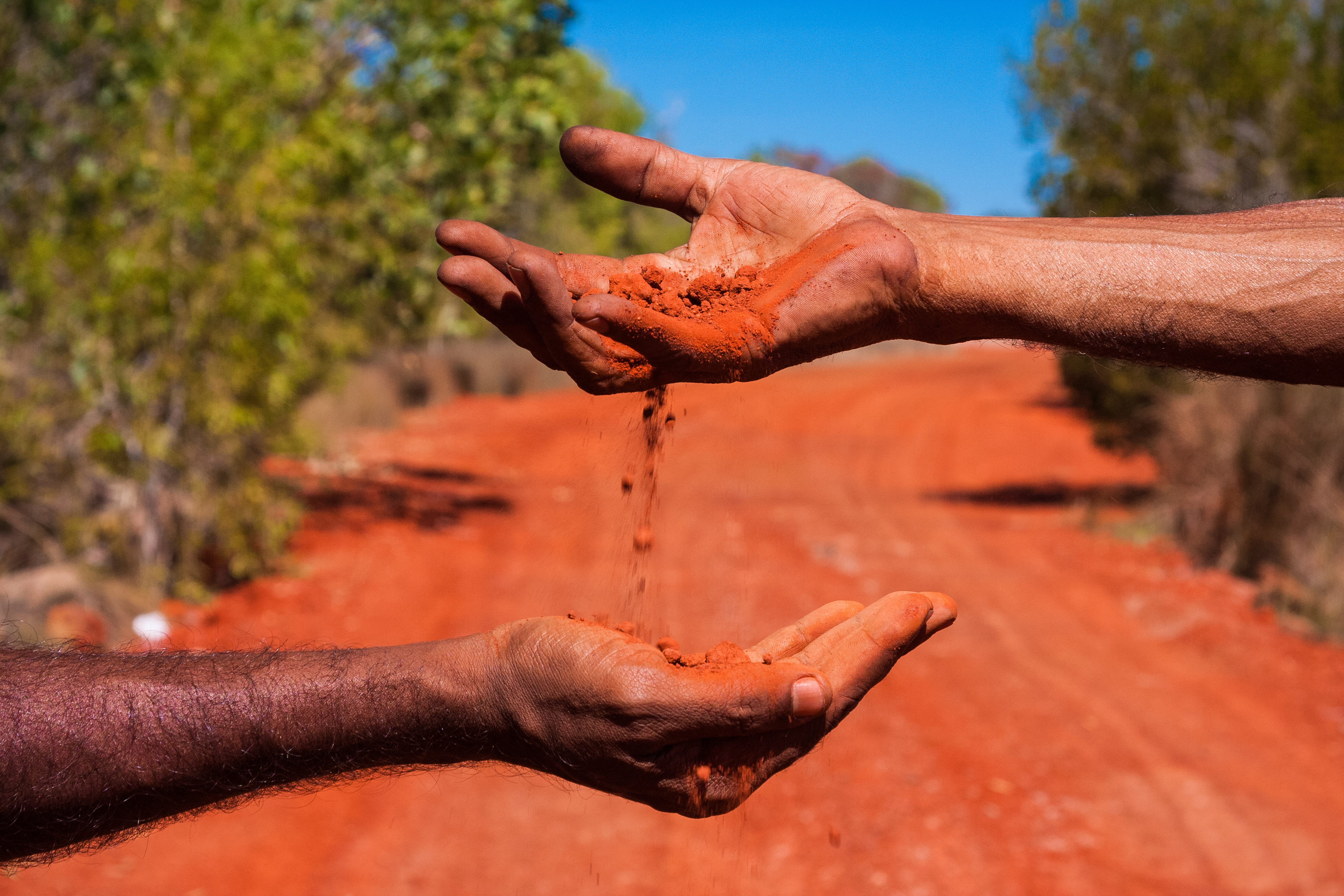 Two Australian Aboriginals sifting red soil through their hands.